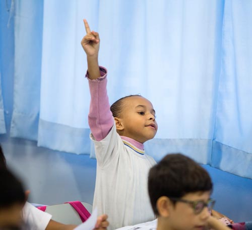 Criança com braço levantado na sala de aula